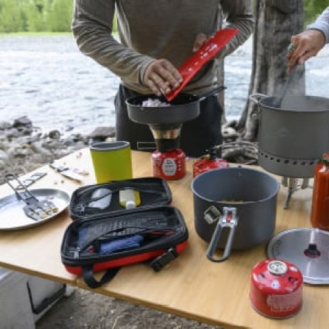 campers making a meal with plates and camp stoves on a table