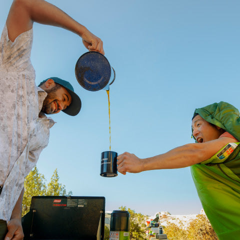a man pouring a cup of coffee into another mans coffee cup while laughing 