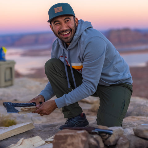 man wearing a blue hoodie while chopping wood in the desert