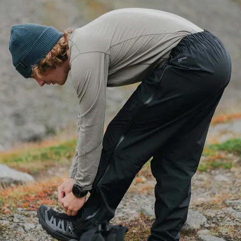 man kneeling over tying his shoes in black outdoor pants