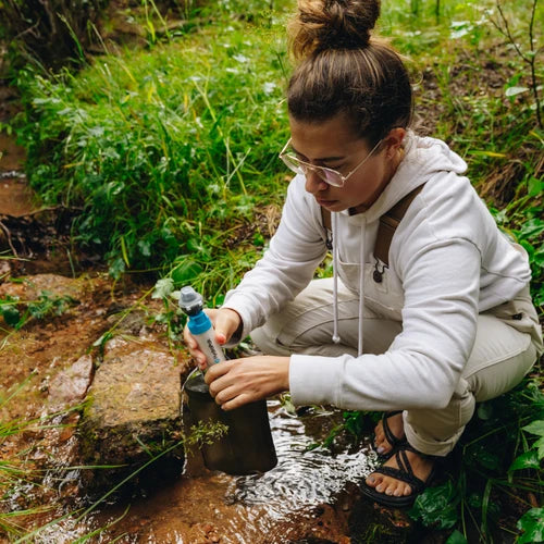 Person filtering water from a stream using a portable filter device in a natural setting.