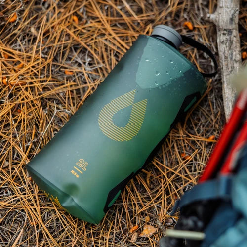 Green water bottle with a logo on a bed of dry leaves