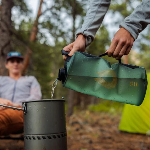 Person pouring water from a green container into a pot outdoors