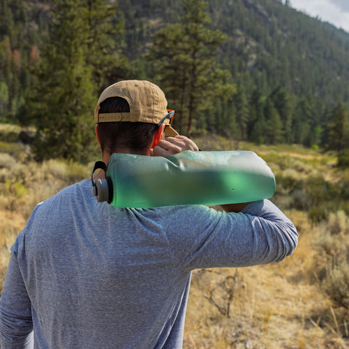Person holding a large green bottle in a forested area