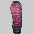 A mummy-style sleeping bag laid flat on a textured beige carpet, featuring a metallic rose-pink center panel and dark gray side panels.
