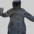 A black quilted puffer jacket with a hood and front zipper, laid flat on a beige carpeted floor. The feet of a person wearing sandals are visible at the bottom edge of the frame.