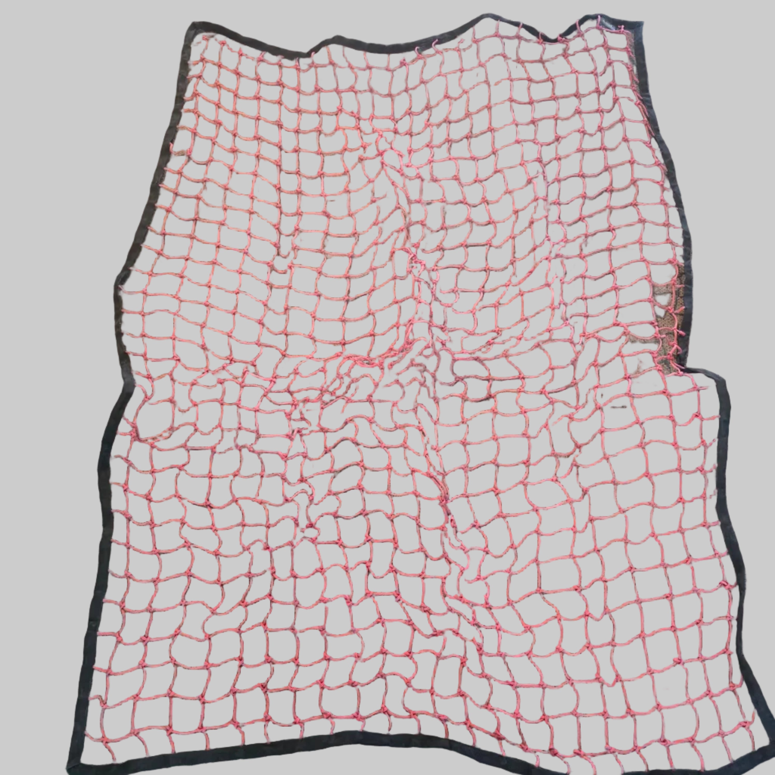 A square black mesh safety net with bright pink cord lines, laid flat on a gray carpeted floor.