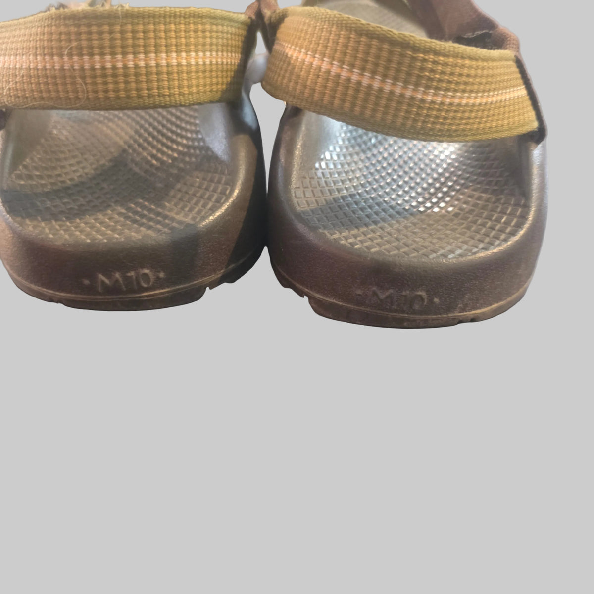A pair of used brown sandals with tan woven straps, shown from the bottom on a dark gray surface.