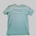 A light blue heathered t-shirt with a small black 'patagonia' logo on the left chest, laid flat on a textured pinkish-brown carpet.