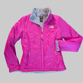 A bright pink quilted puffer jacket with a gray fleece-lined hood and cuffs, laid flat on a brown carpeted floor. The brand logo 'The North Face' is visible on the chest.