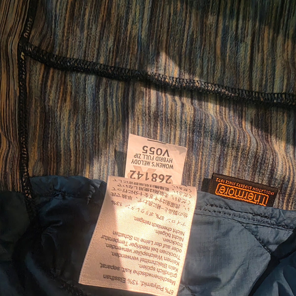 Close-up of the inside of a striped garment showing a sewn-in size label reading 268142 and a black brand tag that appears to read Lomemore, with a blue inner lining and dark zipper visible.