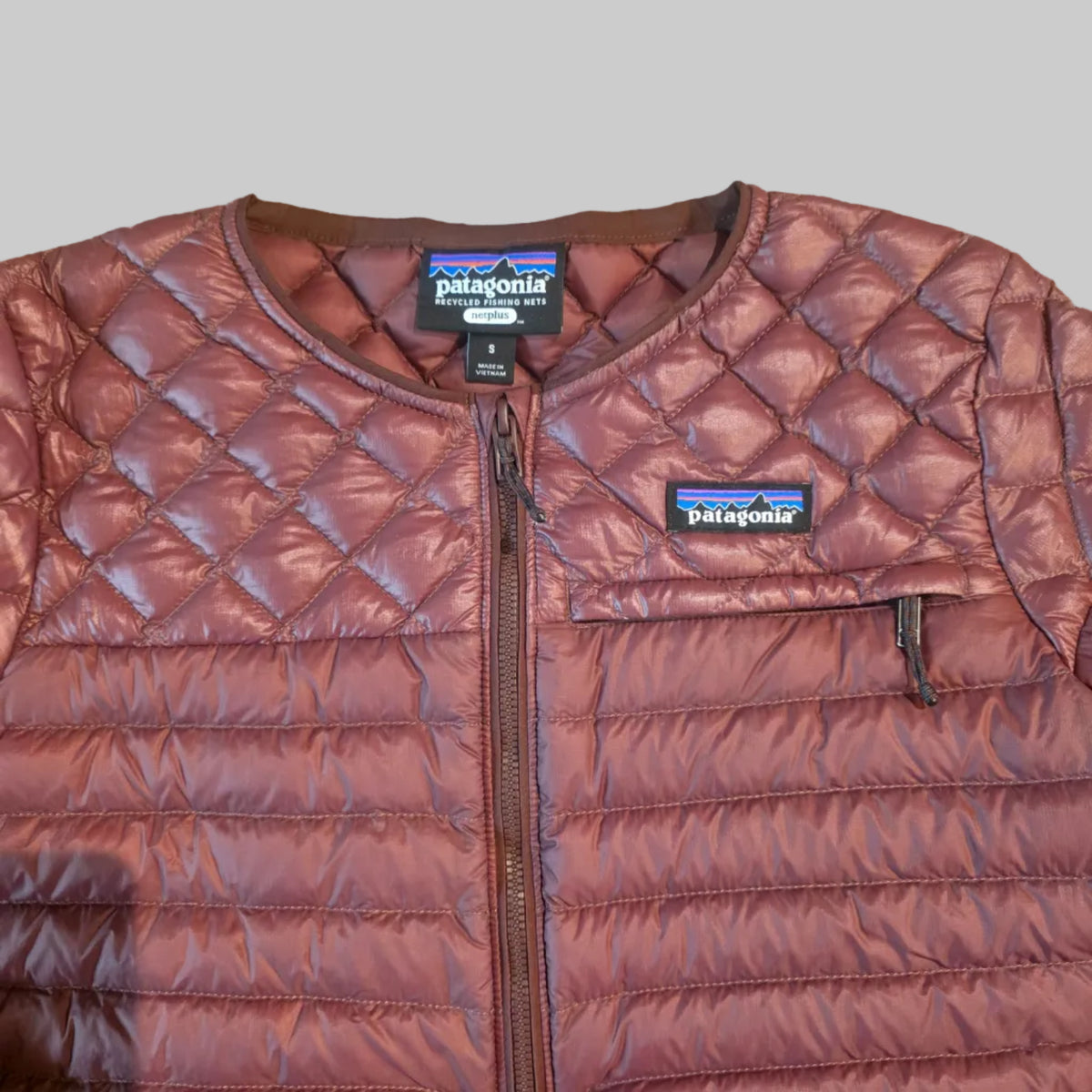 A close-up flat lay of a quilted Patagonia jacket in a dusty rose or mauve-brown color, showing the diamond-stitched pattern, zipper, and Patagonia brand labels.