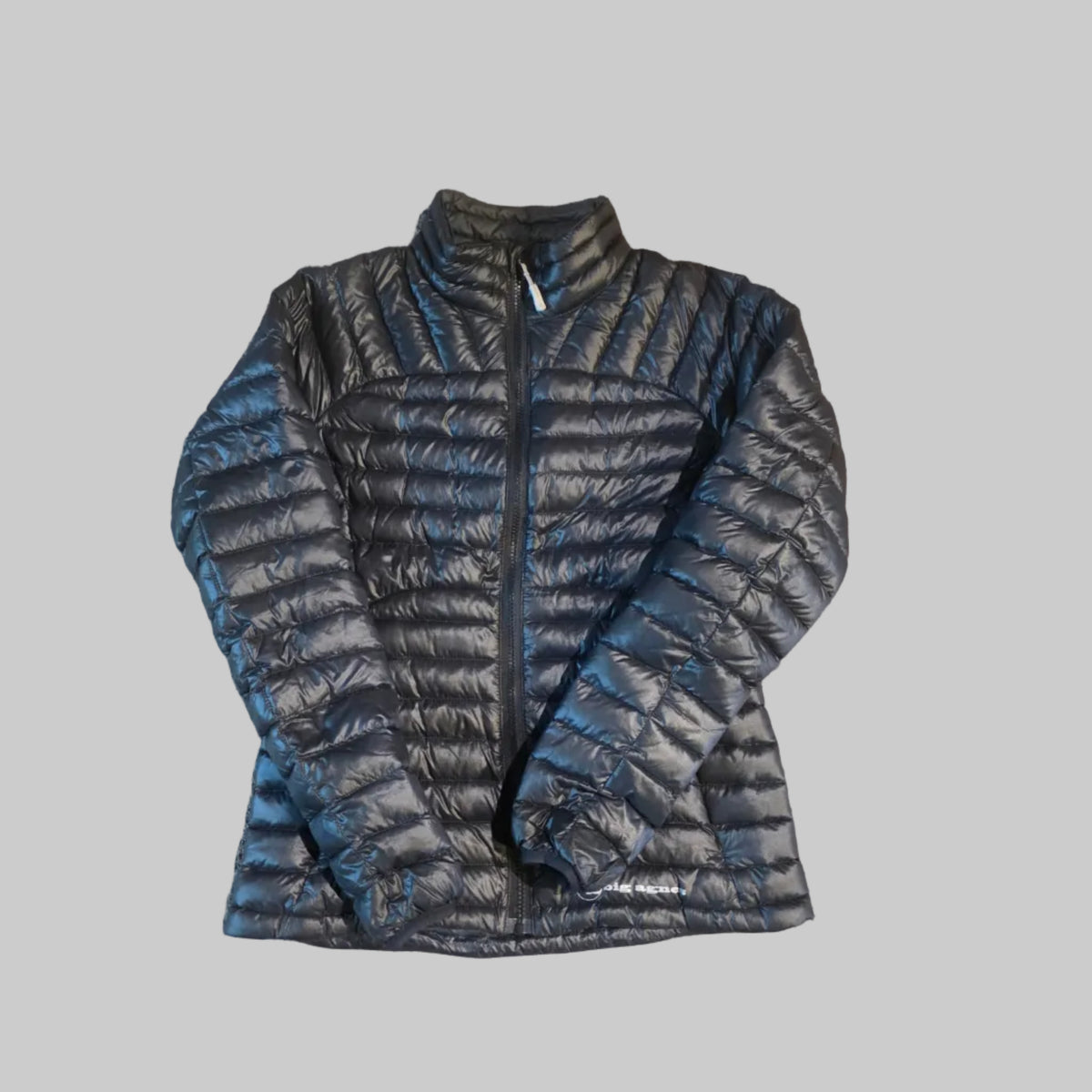 A black quilted puffer jacket laid flat on a textured beige carpet.