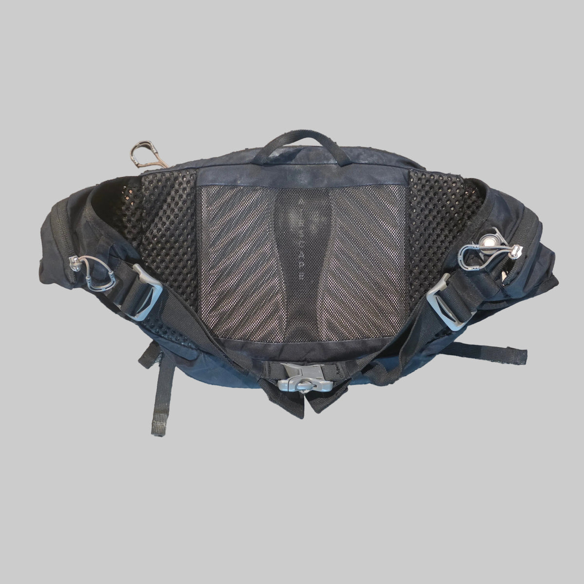A black technical backpacking pack shown from a top-down view, highlighting its breathable mesh back panel and adjustable straps, placed on a textured carpet.