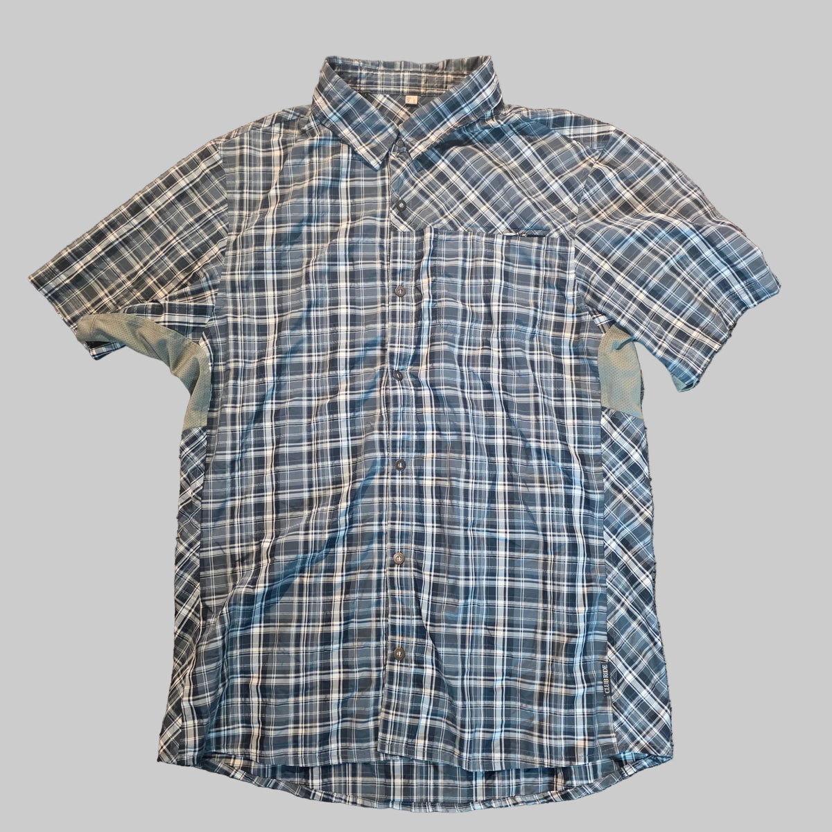 A short-sleeve button-up plaid shirt in blue, white, and gray, laid flat on a textured carpet.