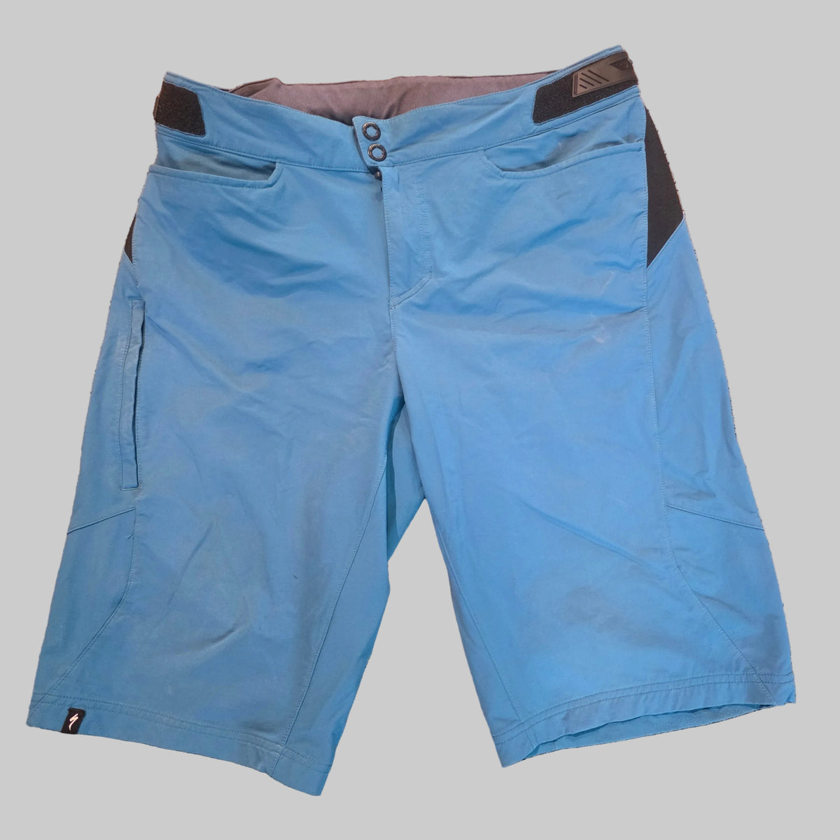 Blue mountain biking shorts with black side panel accents and a gray inner waistband, laid flat on a speckled brown carpet.
