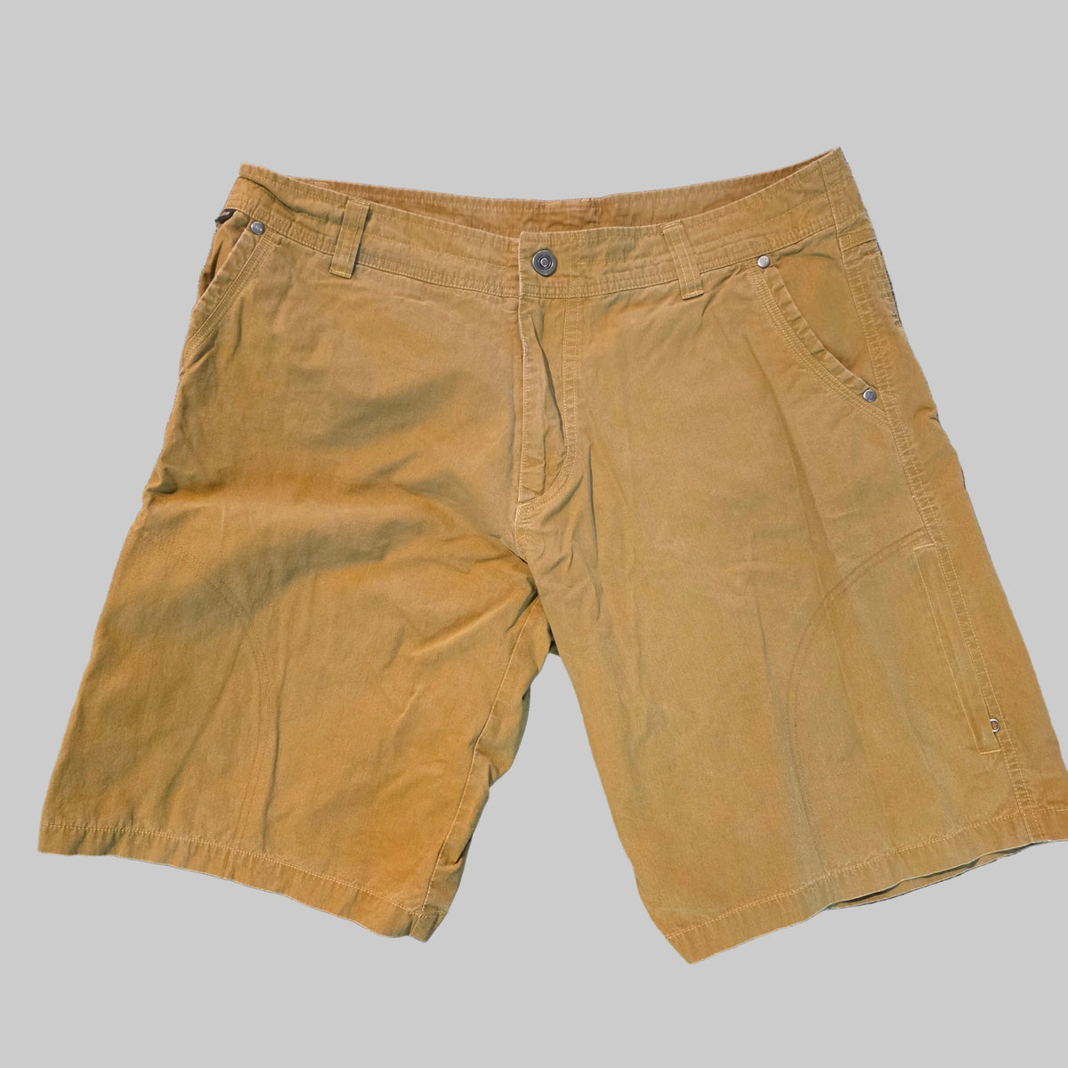 A pair of men's tan corduroy shorts laid flat on a gray carpeted floor.