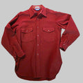 A long-sleeve button-up shirt in a deep red or burgundy color, laid flat on a textured gray carpet. The shirt features two buttoned chest pockets and a pointed collar.