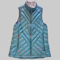 A teal blue diamond-quilted puffer vest with a high stand-up collar, front zipper, and zippered side pockets, laid flat on a textured pinkish-brown carpet. The brand name 'Marmot' is visible in red text near the bottom right hem.