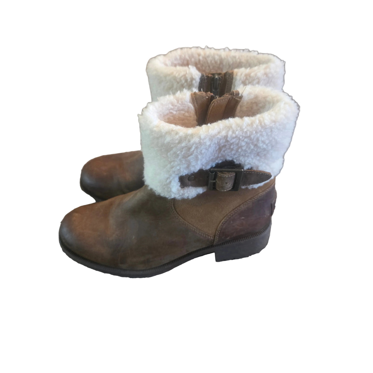 A pair of brown leather ankle boots with thick white sherpa fleece cuffs and side buckle straps, resting on a textured gray carpet.