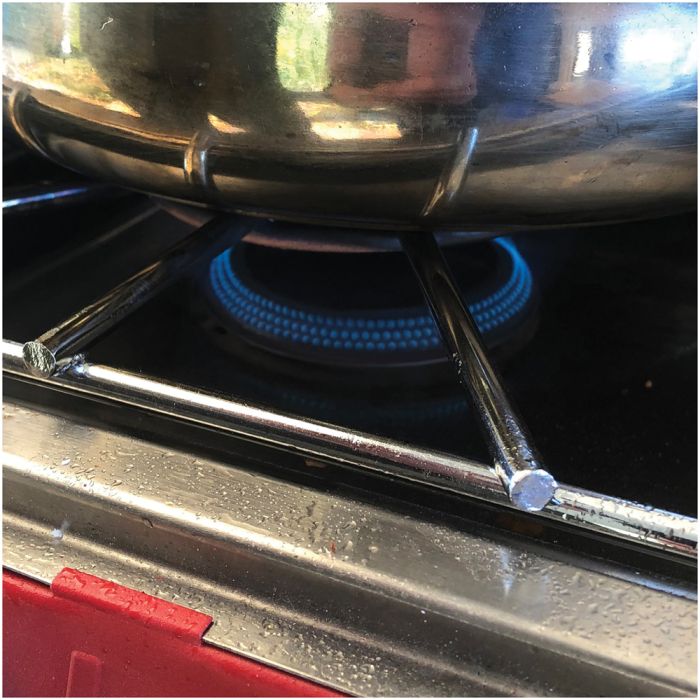 Close-up of a stainless steel pot sitting on a gas stove burner with a blue flame visible underneath.