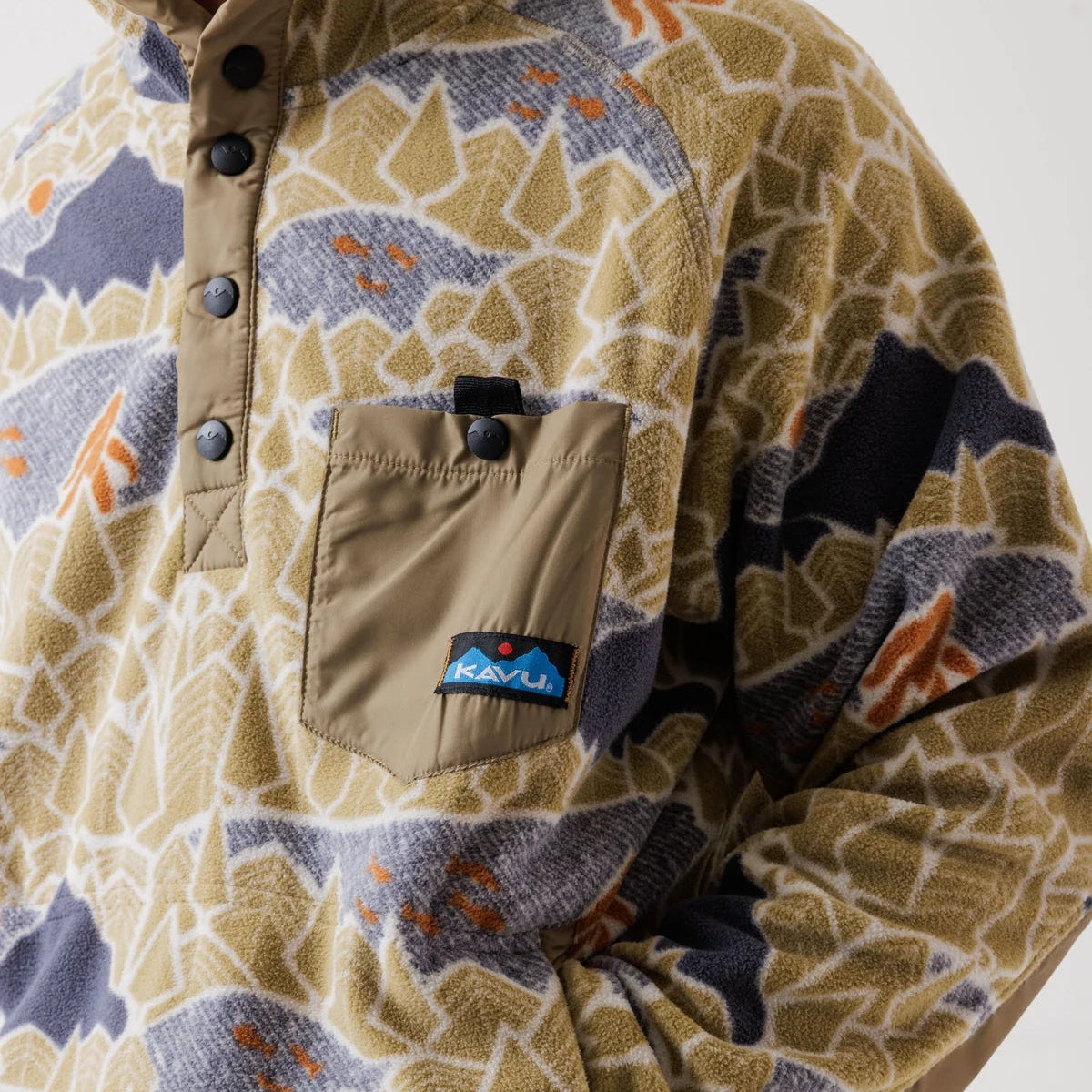 Close-up of a Patagonia fleece pullover with a beige, gray, and orange geometric pattern, featuring a brown buttoned chest pocket with a Patagonia logo patch.