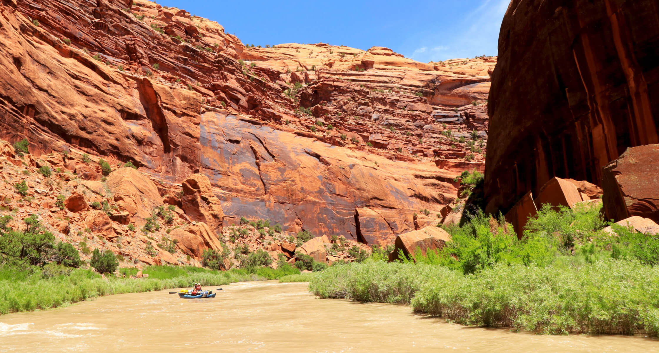 River scene with red rock cliffs and greenery