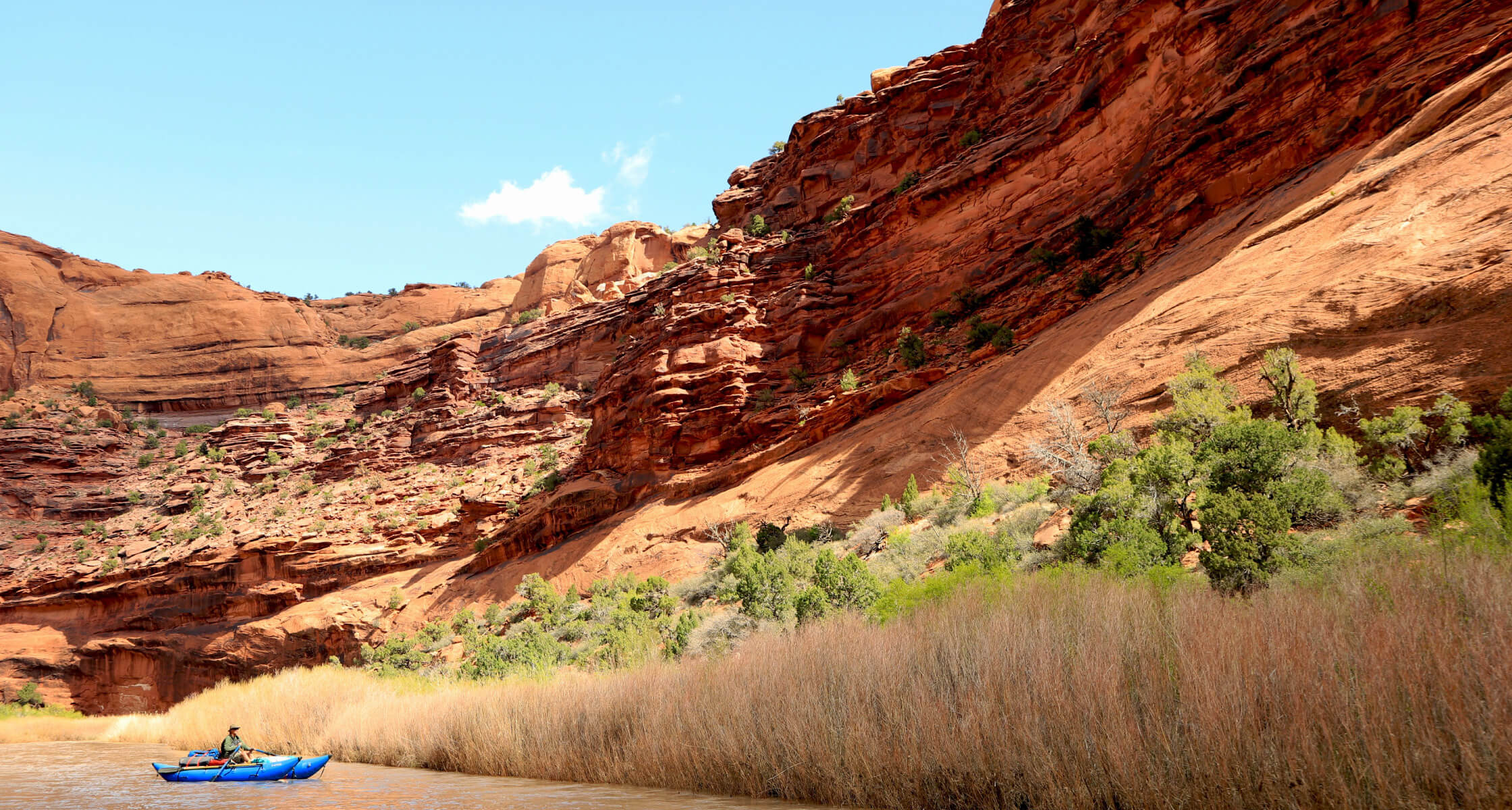 Kayakers on a river with red rock cliffs and greenery