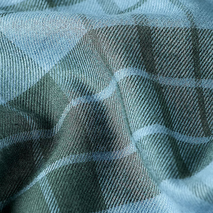 A close-up of a plaid fabric with a textured weave, featuring intersecting stripes of light blue, dark green, and gray.