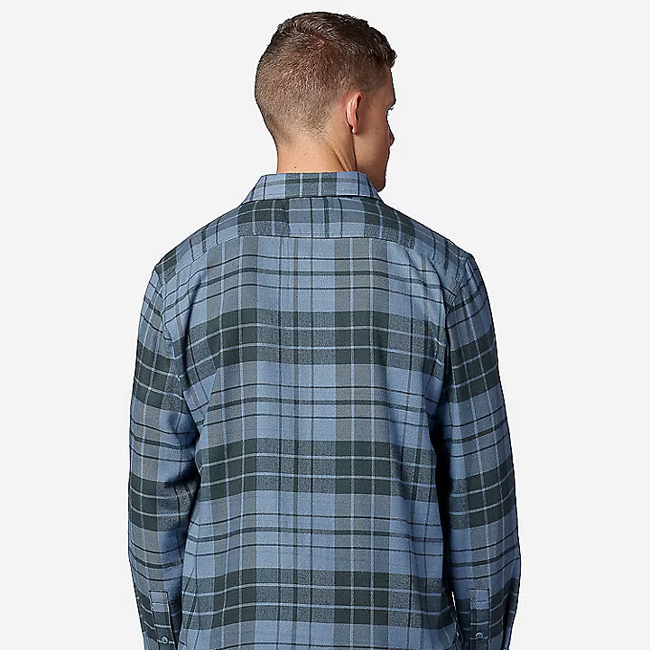 A man viewed from the back wearing a blue and green plaid button-down shirt and dark pants, set against a plain light gray background.