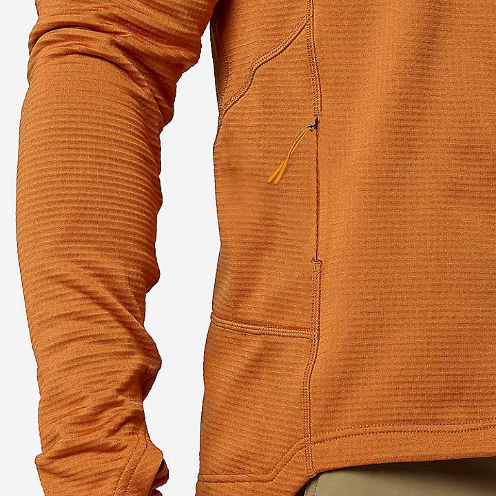 Close-up of a person wearing a textured orange long-sleeve fleece or pullover top with a zip pocket and tan pants. The Marmot logo is visible on the pants.