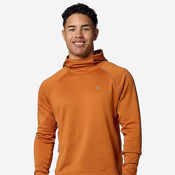 A smiling man wearing a textured orange hooded long-sleeve athletic top and khaki pants, standing against a light gray studio background.