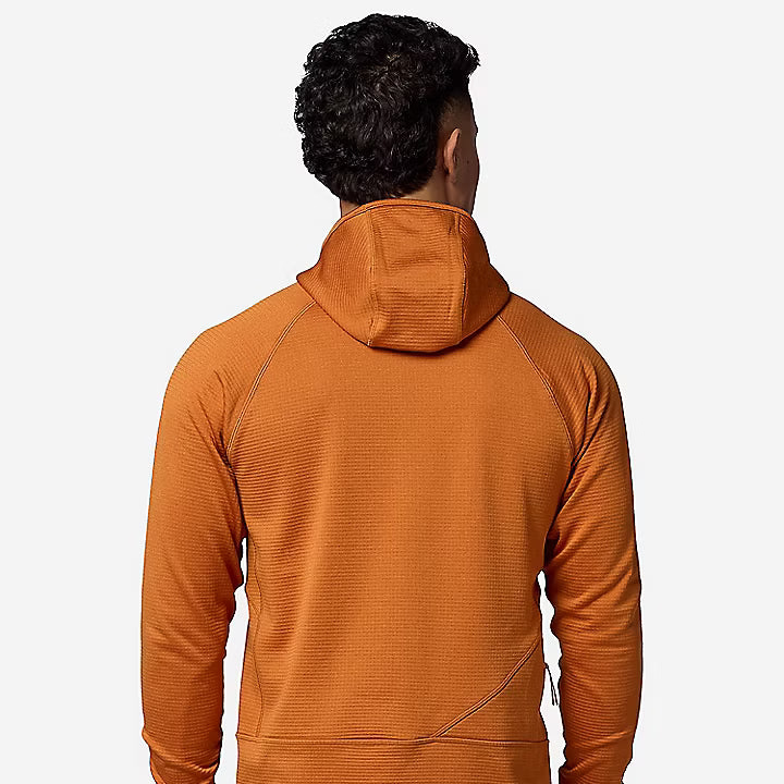 A man viewed from behind wearing a textured orange hooded long-sleeve athletic top and khaki pants against a light gray studio background.