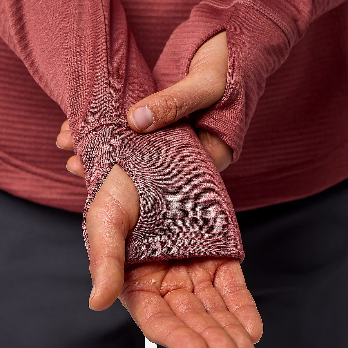 Close-up of a person wearing a ribbed long-sleeve top in a dusty rose color, demonstrating a thumbless wrist cuff with the thumb pulled out.