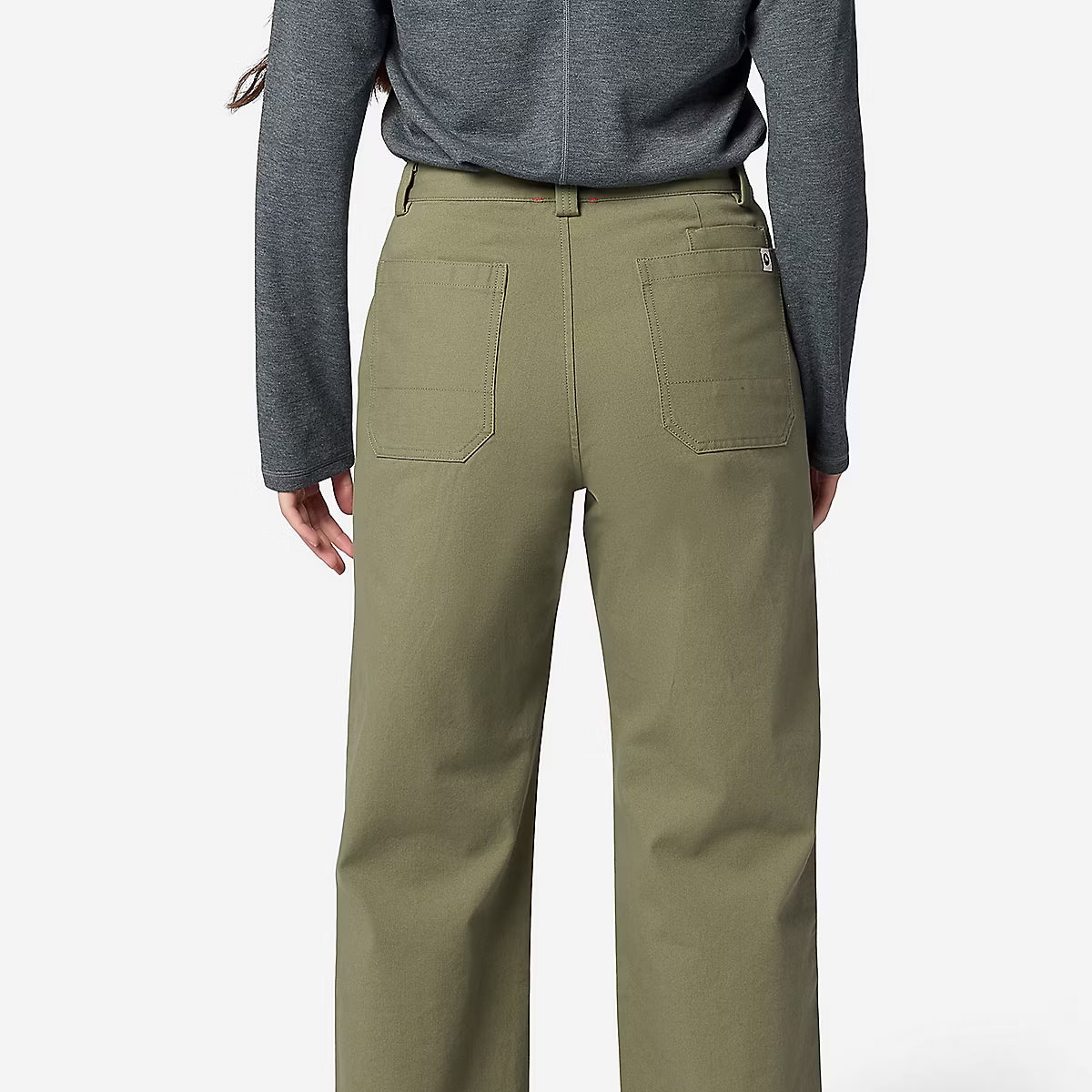 A person shown from the back wearing olive green wide-leg pants, a gray long-sleeve top, and beige shoes against a light gray studio background.