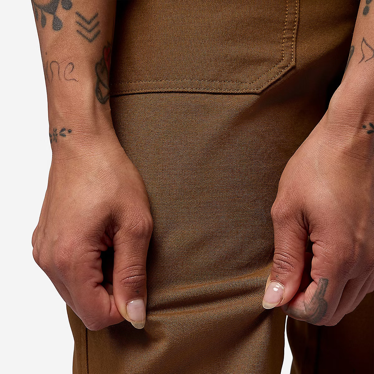 Close-up of a person wearing brown pants, pulling the fabric slightly to show the stretch and texture of the material.