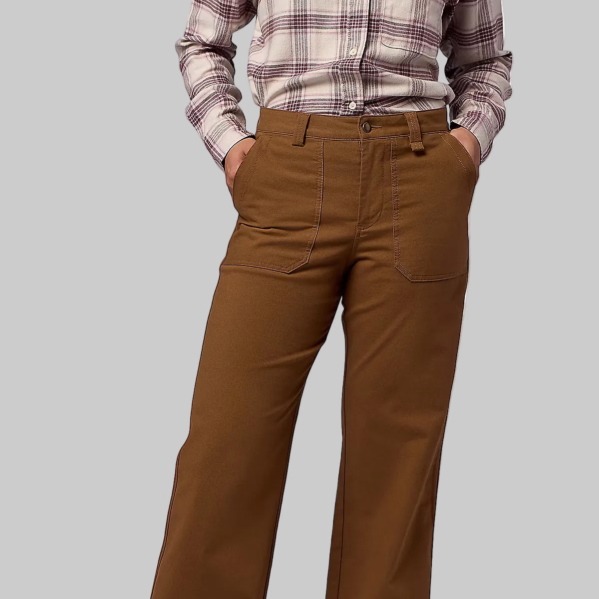 A person wearing brown wide-leg pants, a pink and white plaid shirt, and beige sneakers, standing against a light gray studio background.